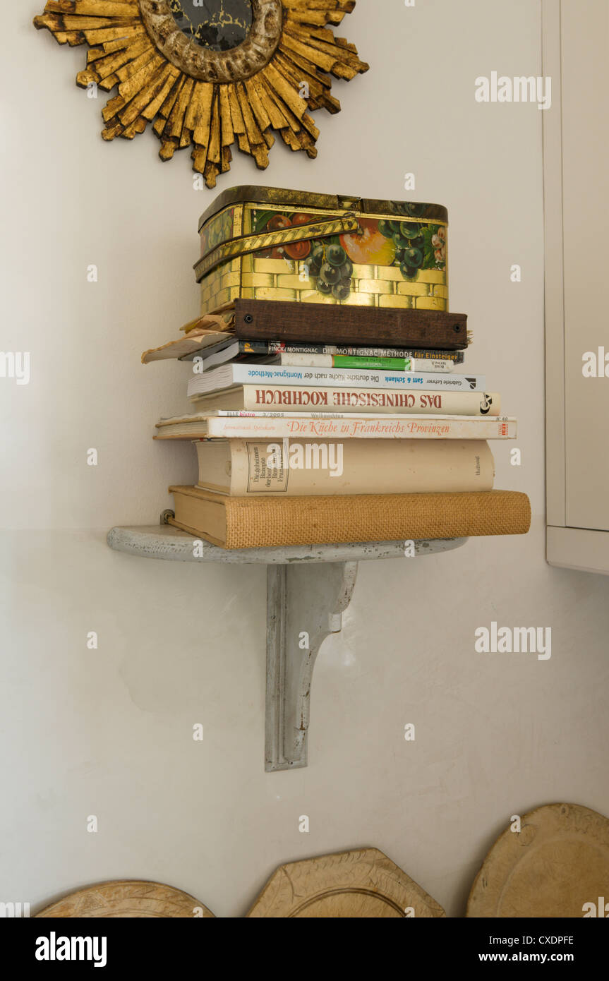 Stack of books and sewing basket on wall-mounted shelf Stock Photo