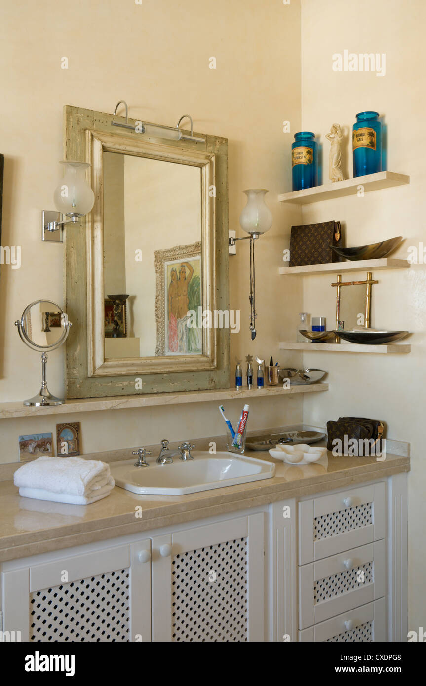 Wash basin below rectangular mirror in bathroom with wall shelving Stock Photo