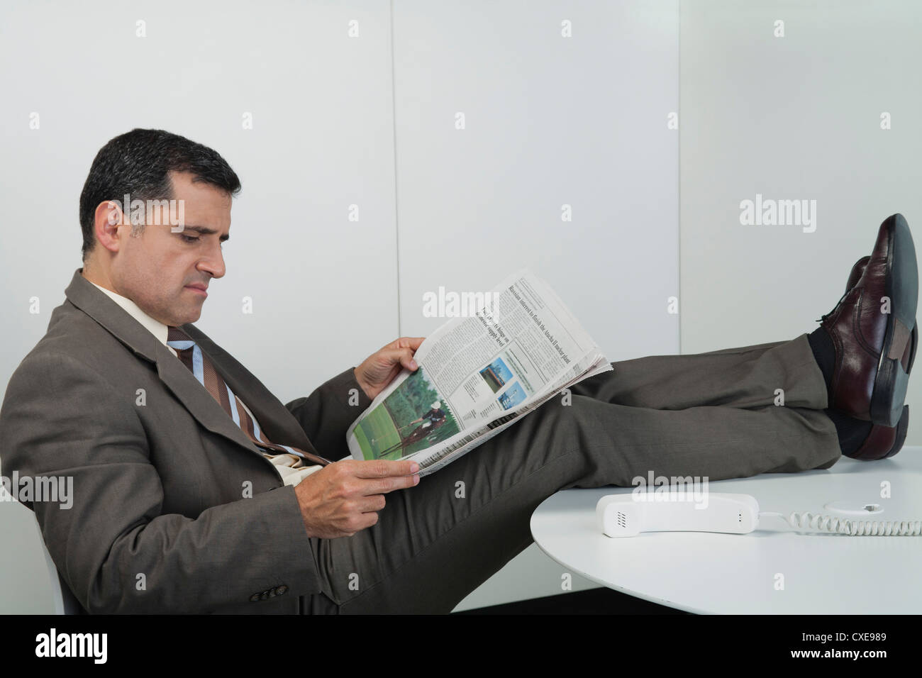 Businessman Reading Newspaper In Office With Feet Up On Desk