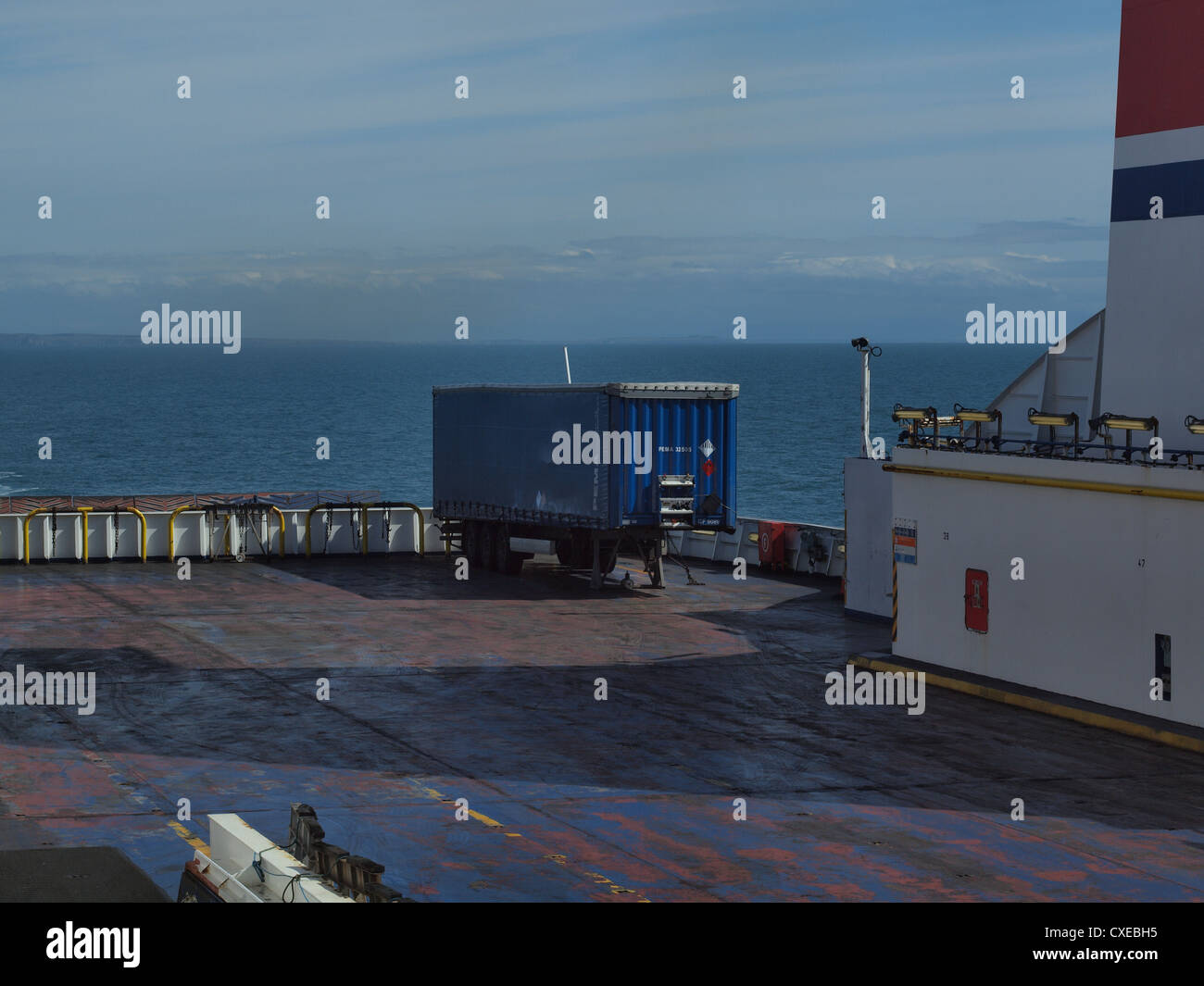Container-side trucks trailor a stern on board a ship, as the vessel plies through the Irish sea on a clear day. Stock Photo