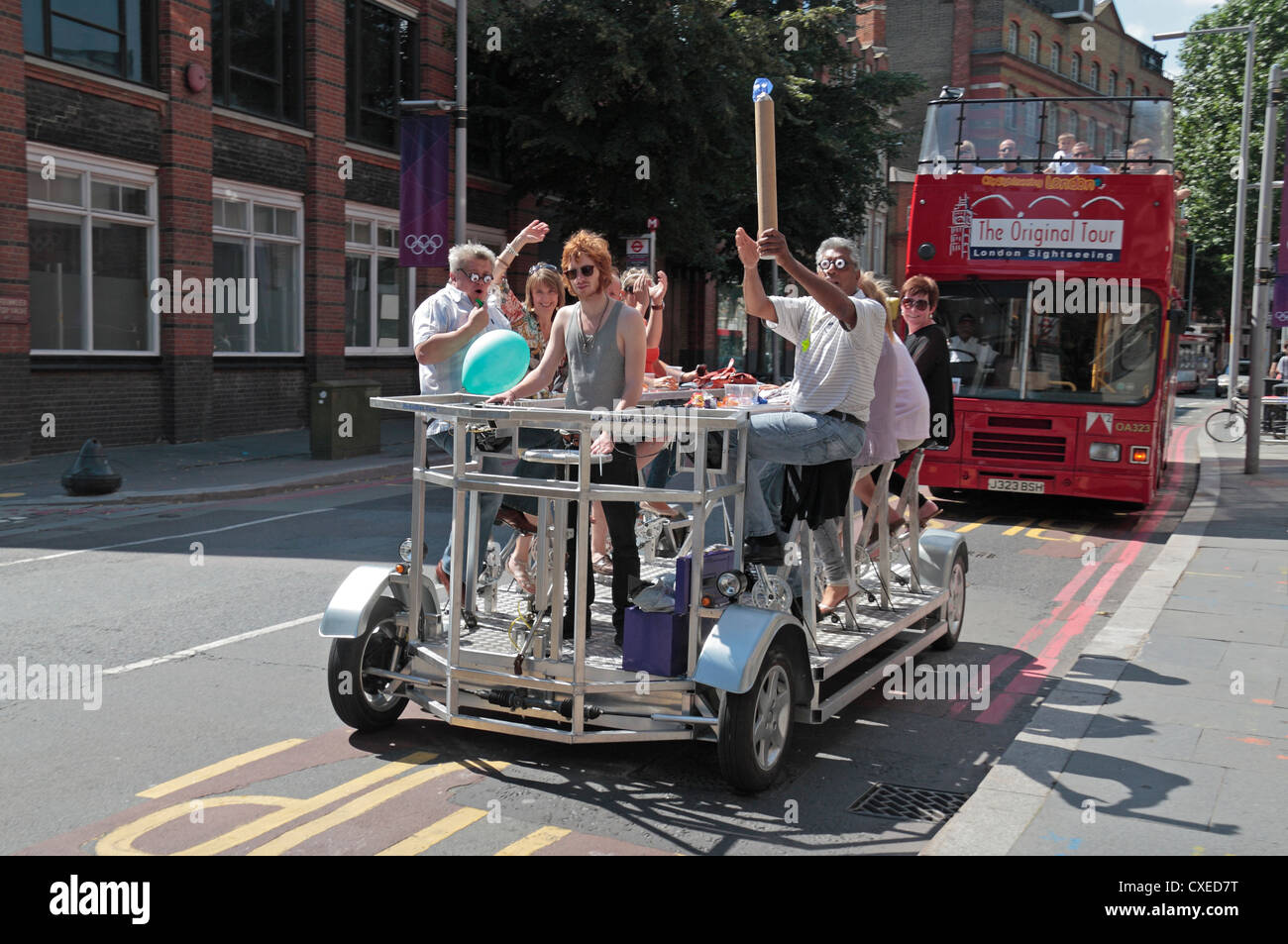 Tourists cycling on a Pedibus, a party cycling experience in London, UK.  Behind in a more traditional open topped bus tour. Stock Photo