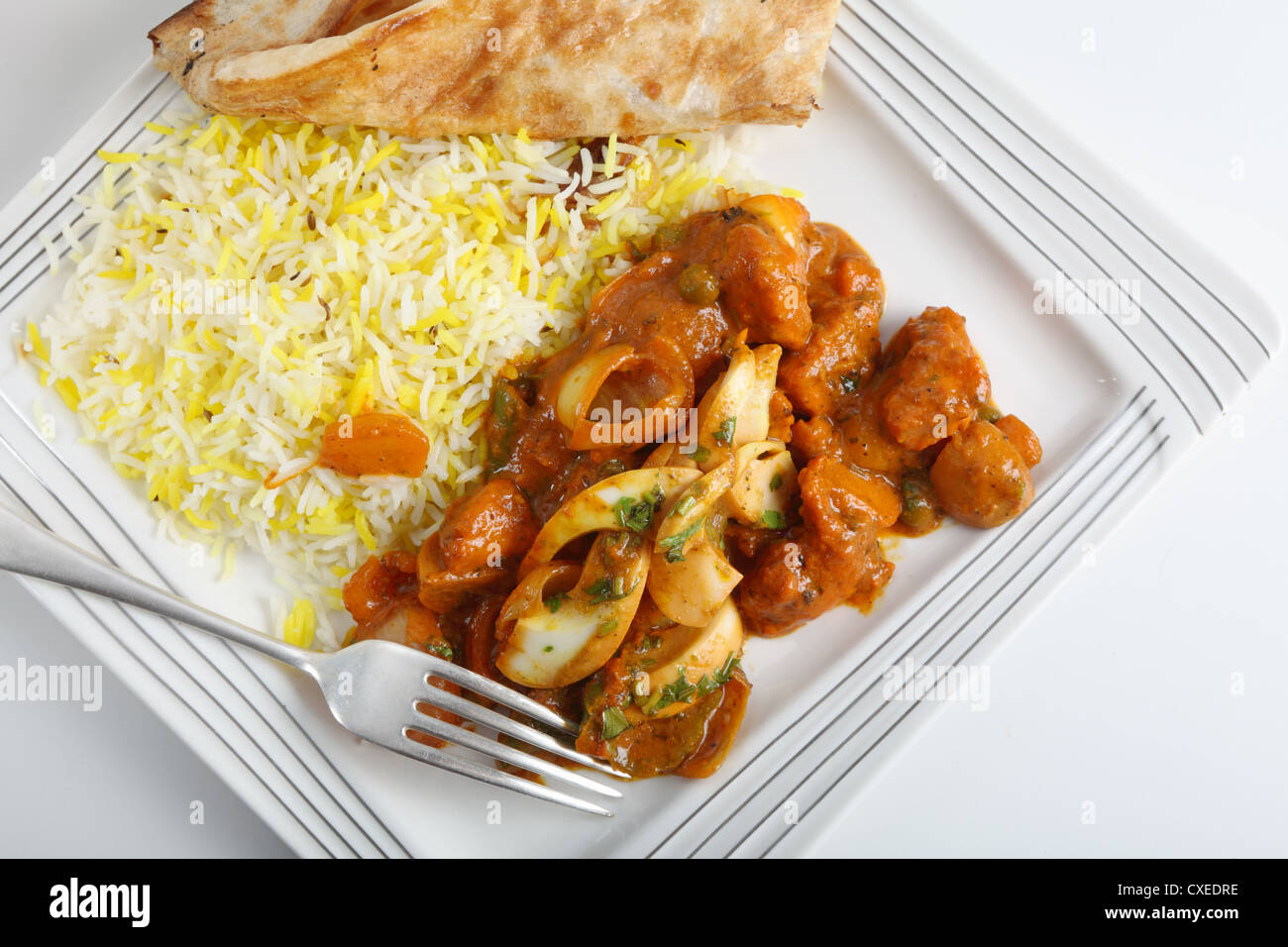 Chicken jalfrezi curry on a plate with pilau rice, a piece of naan bread and a fork from above. Stock Photo