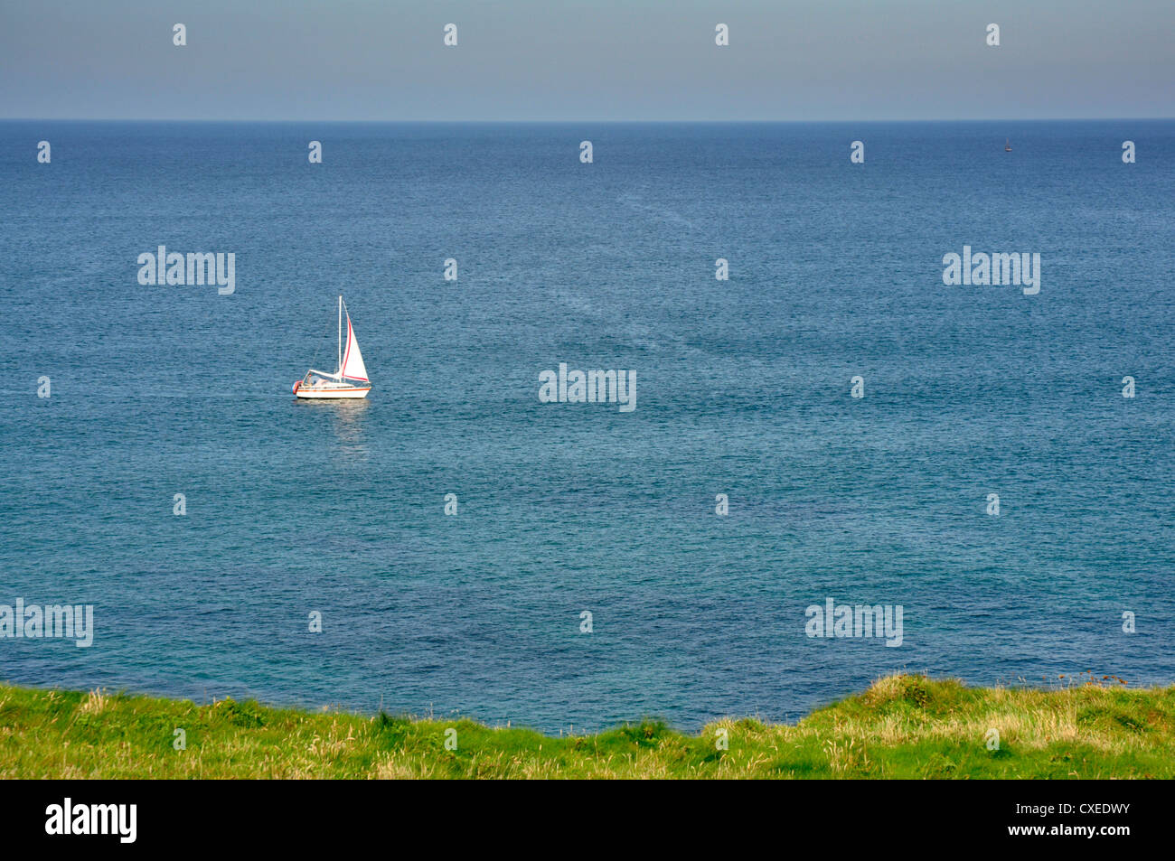 Azure sea - white sail on a small boat - green cliff top - sailing - alone on a empty seascape - a summer day Stock Photo