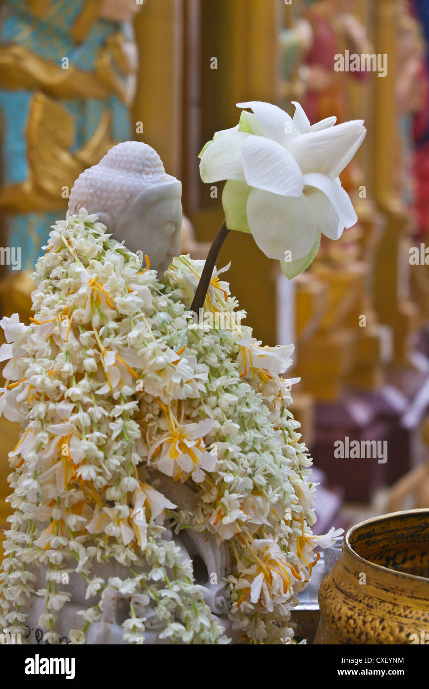 A BUDDHA STATUE is covered with flowers by followers at the SHWEDAGON PAYA or PAGODA which dates from 1485 - YANGON, MYANAMAR Stock Photo