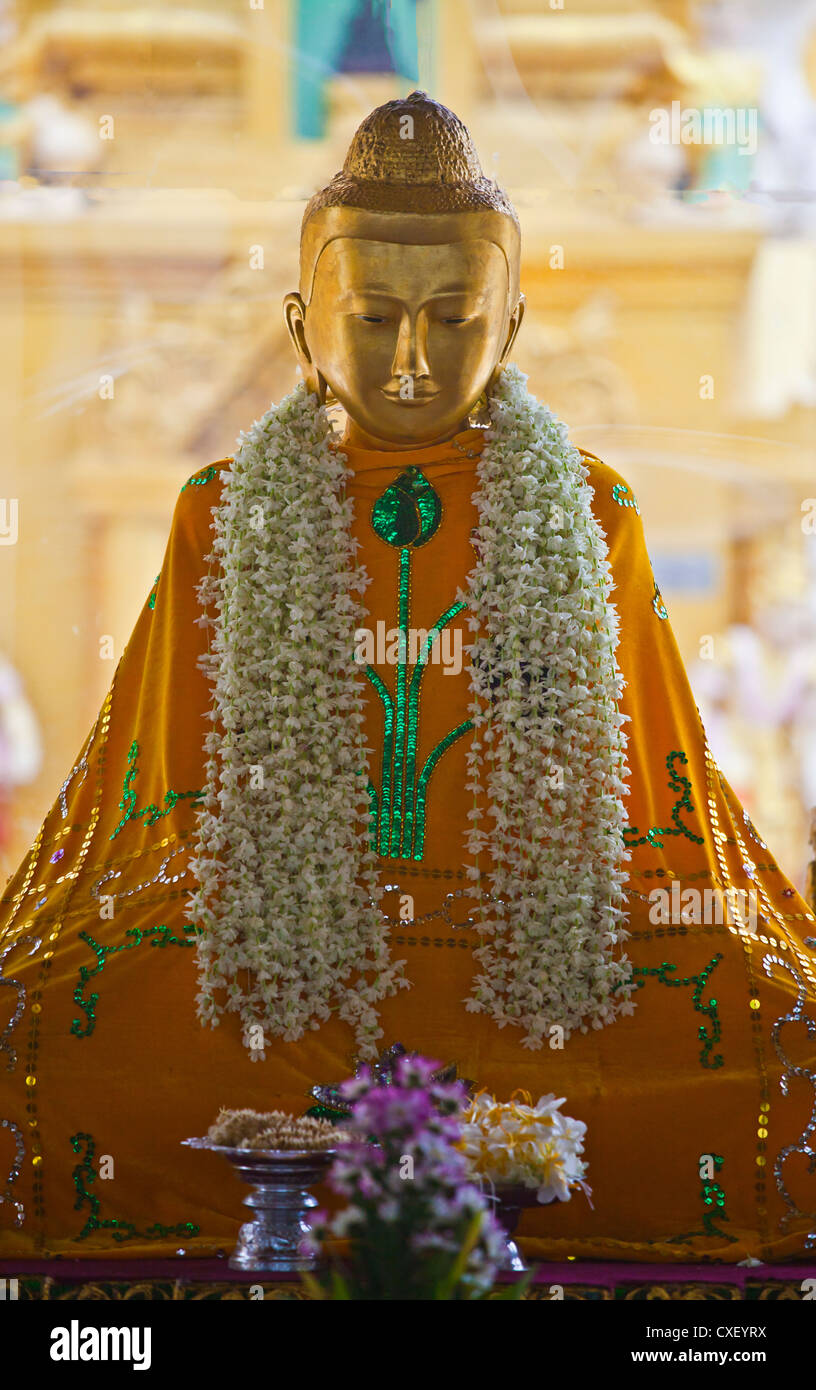 A BUDDHA STATUE adorned with flowers at the SHWEDAGON PAYA or PAGODA which dates back to the time of Buddha - YANGON, MYANMAR Stock Photo