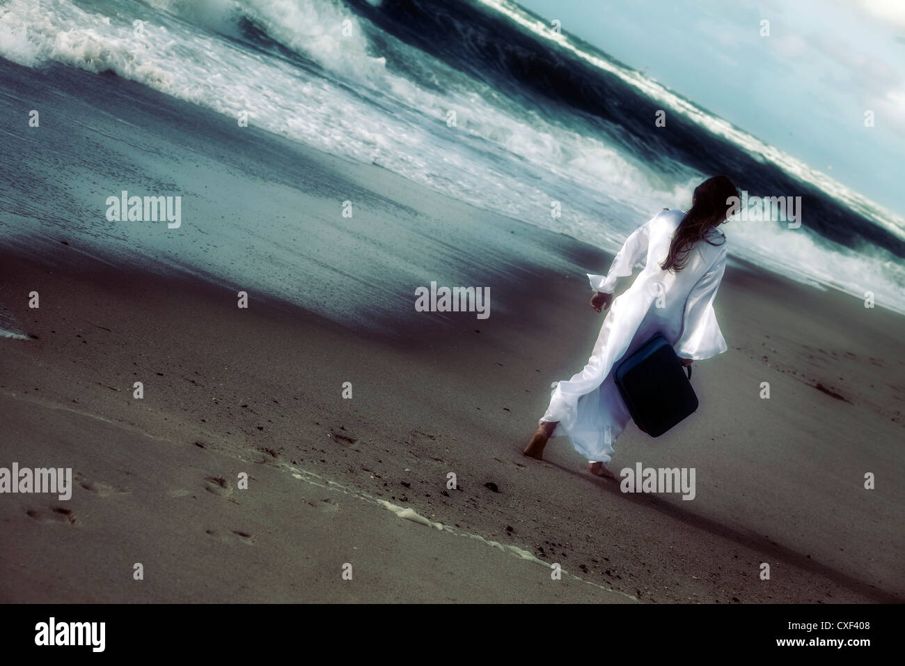 a girl in a white dress at the sea with a suitcase Stock Photo