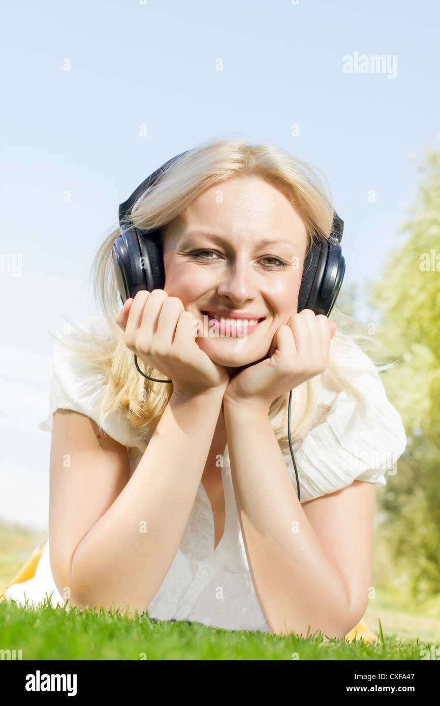 Happiness blonde woman with headphones relaxing on green grass in the ...