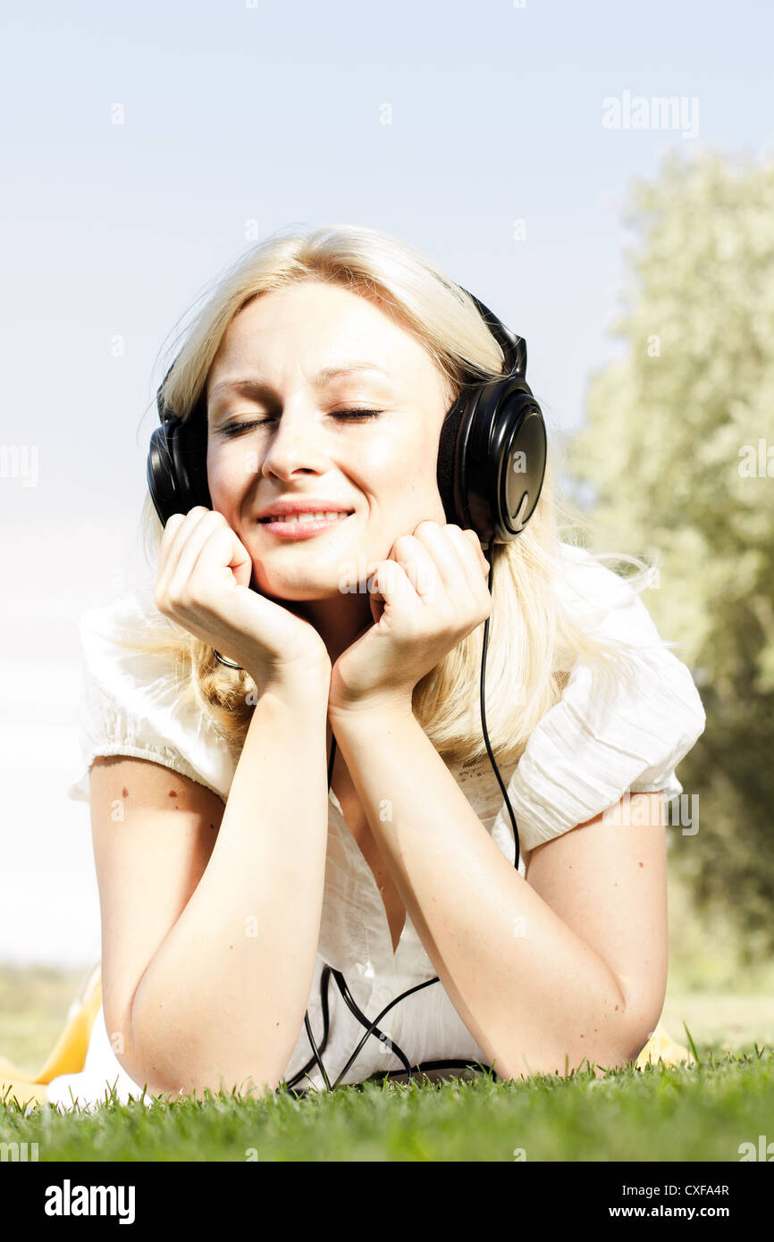Happiness blonde woman with headphones relaxing on green grass in the ...