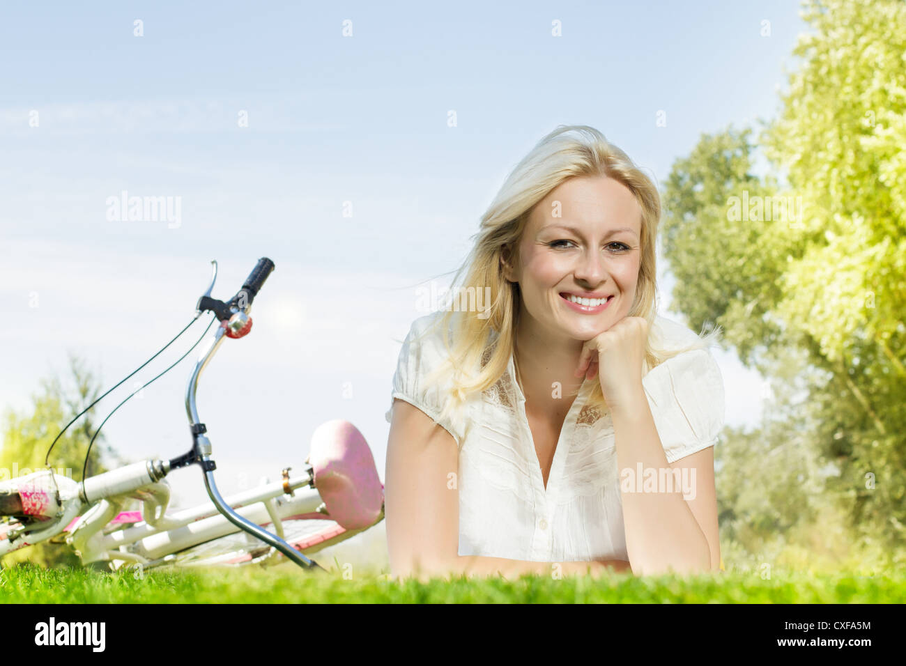 Happiness young blond woman relaxing on green grass after cycling ...