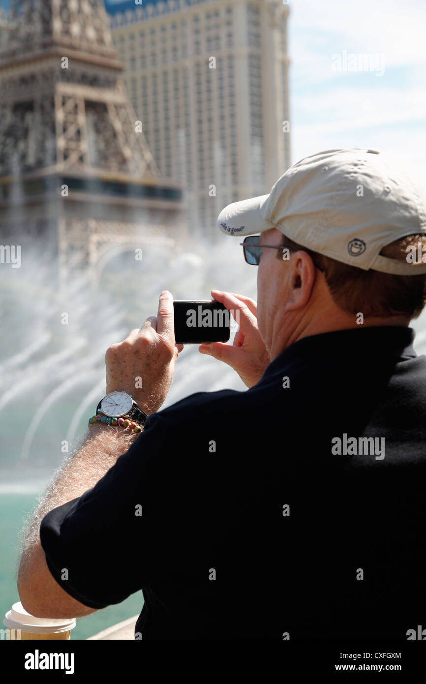 60ish Man Photographing the Water Fountain Show at the Bellagio Hotel, Las Vegas, NV, using his iPhone. Stock Photo