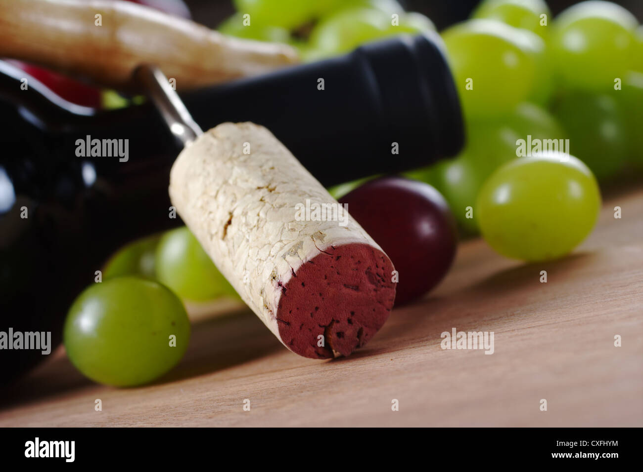 Cork on corkscrew leaning against a wine bottle surrounded by grapes Stock Photo