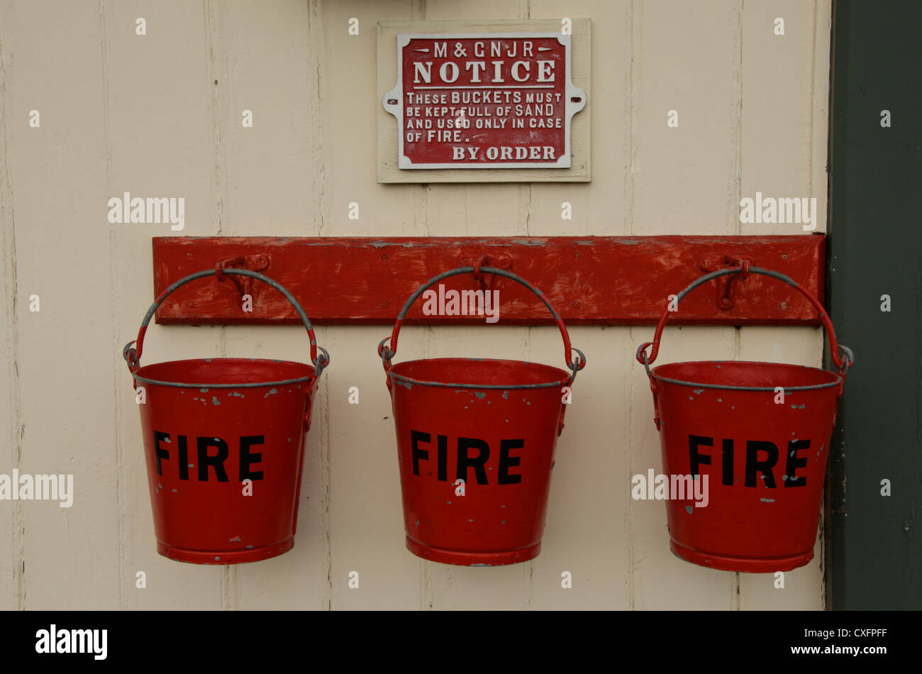 Three fire buckets filled with sand hang in a line ready to use in the event of a fire. Stock Photo