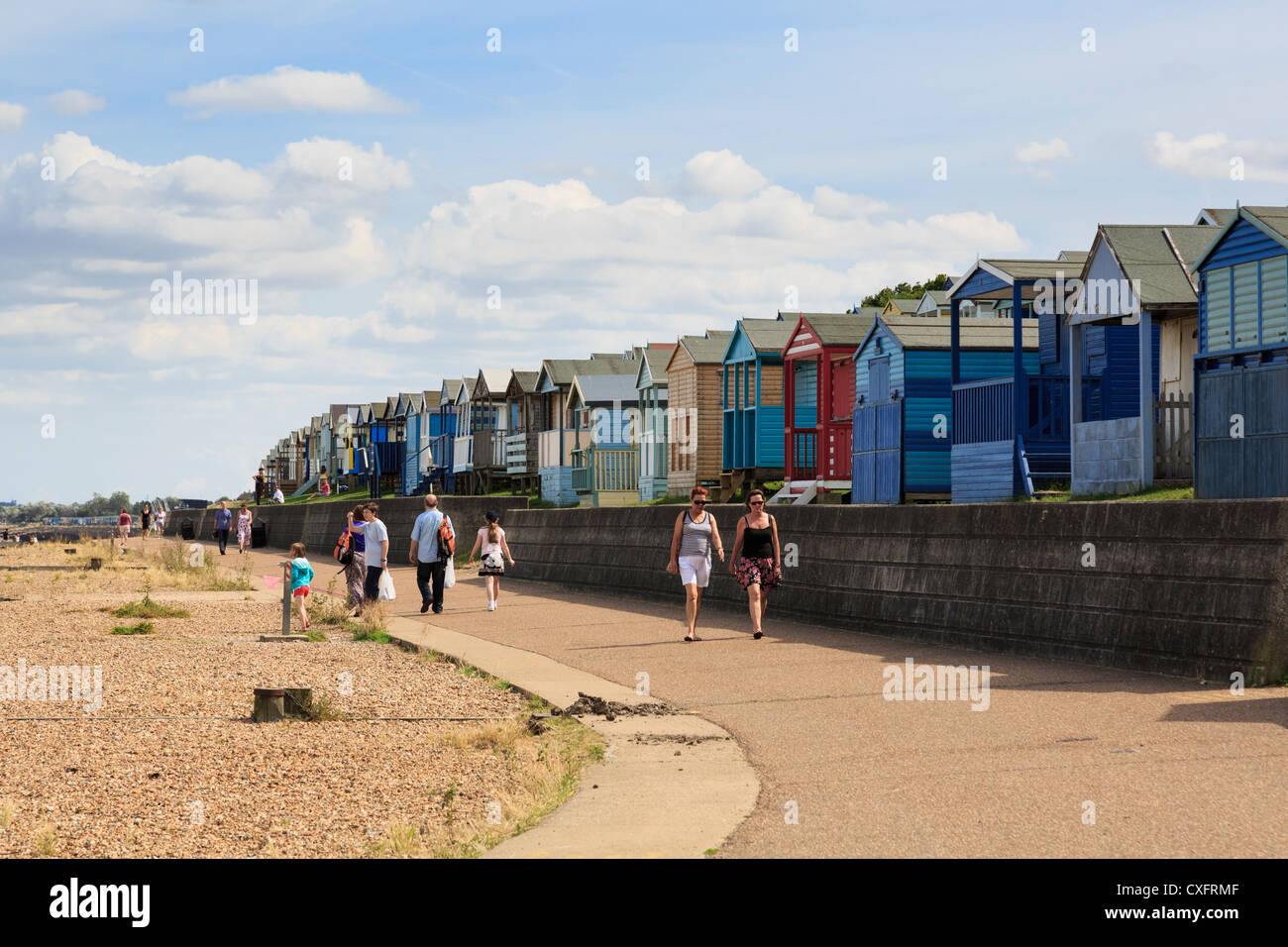 People walking on Whitstable seafront promenade beside beach huts on