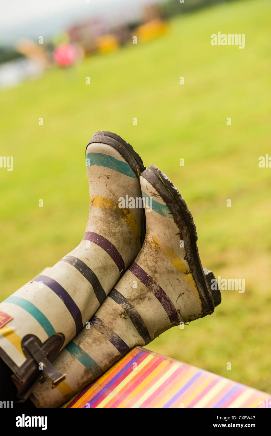 Muddy dirty  'wellies' wellington boots of a person sitting in a deckchair at 'the big tribute' music festival, UK Stock Photo
