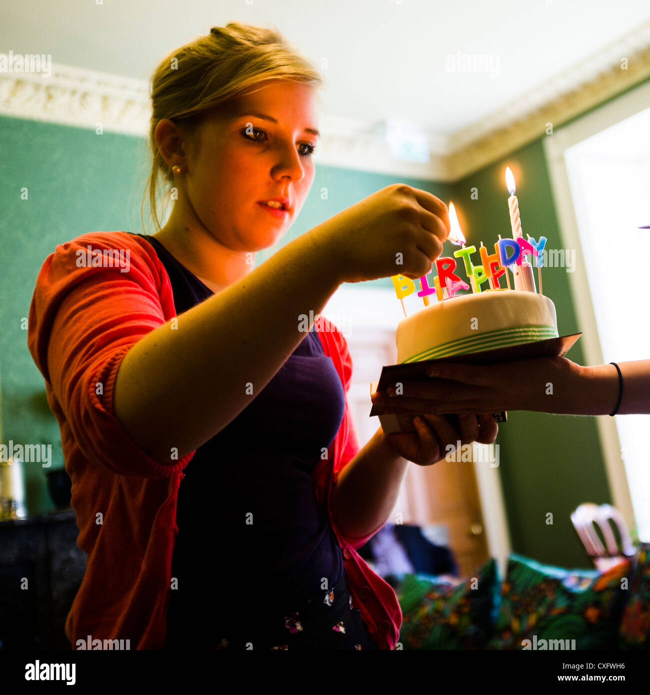 A woman lighting happy birthday party candles on a cake, UK Stock Photo