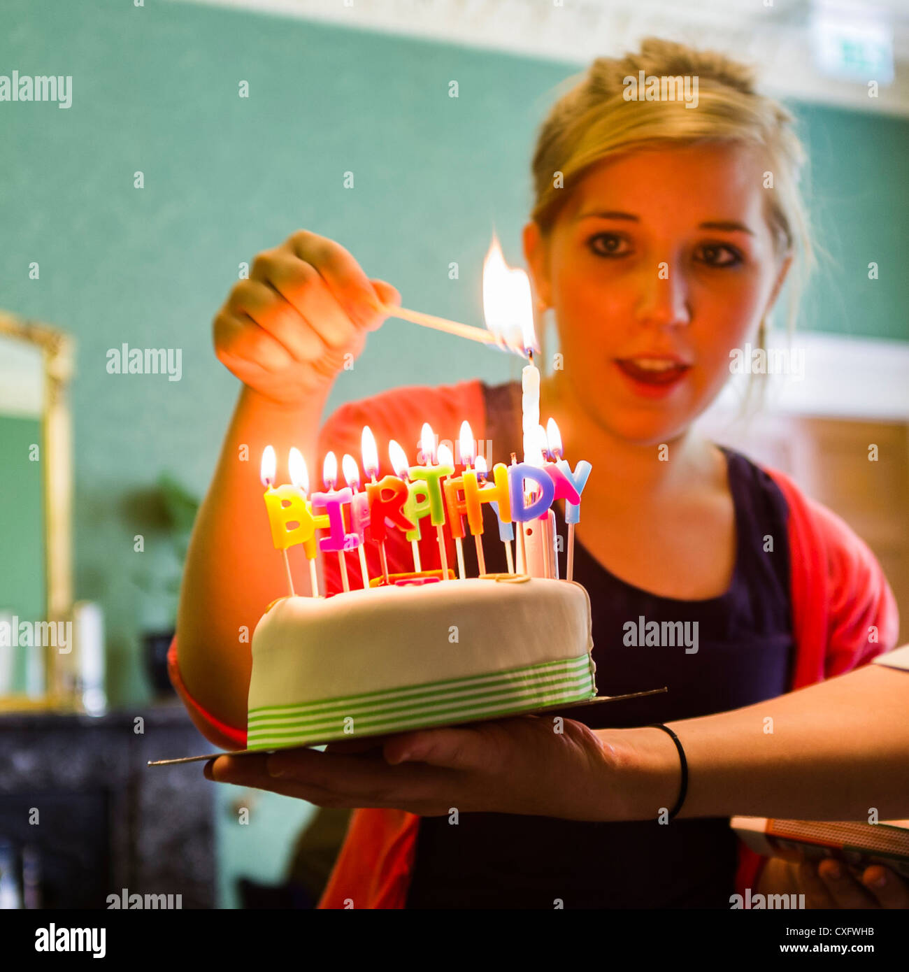 A woman lighting happy birthday party candles on a cake, UK Stock Photo
