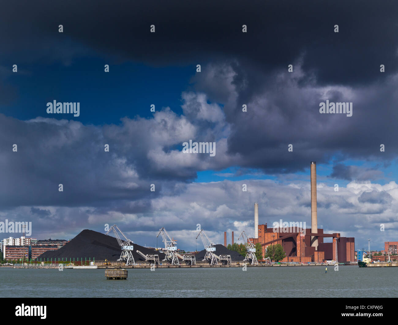 Coal fired power station fossil fuel technology, illuminated by dramatic sky with lake in foreground Helsinki Finland Stock Photo