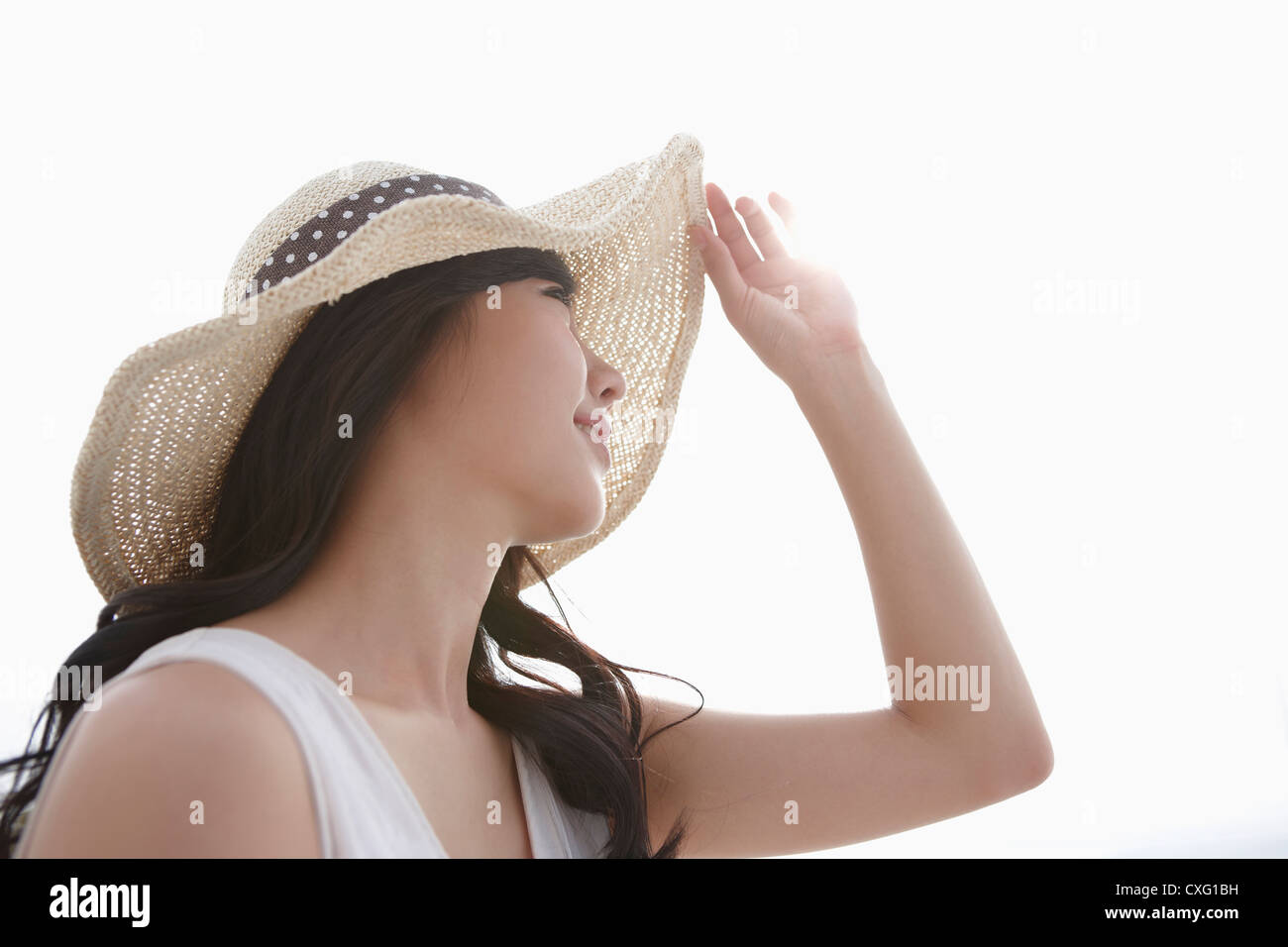 A woman wearing a white dress and straw hat posing in white background ...