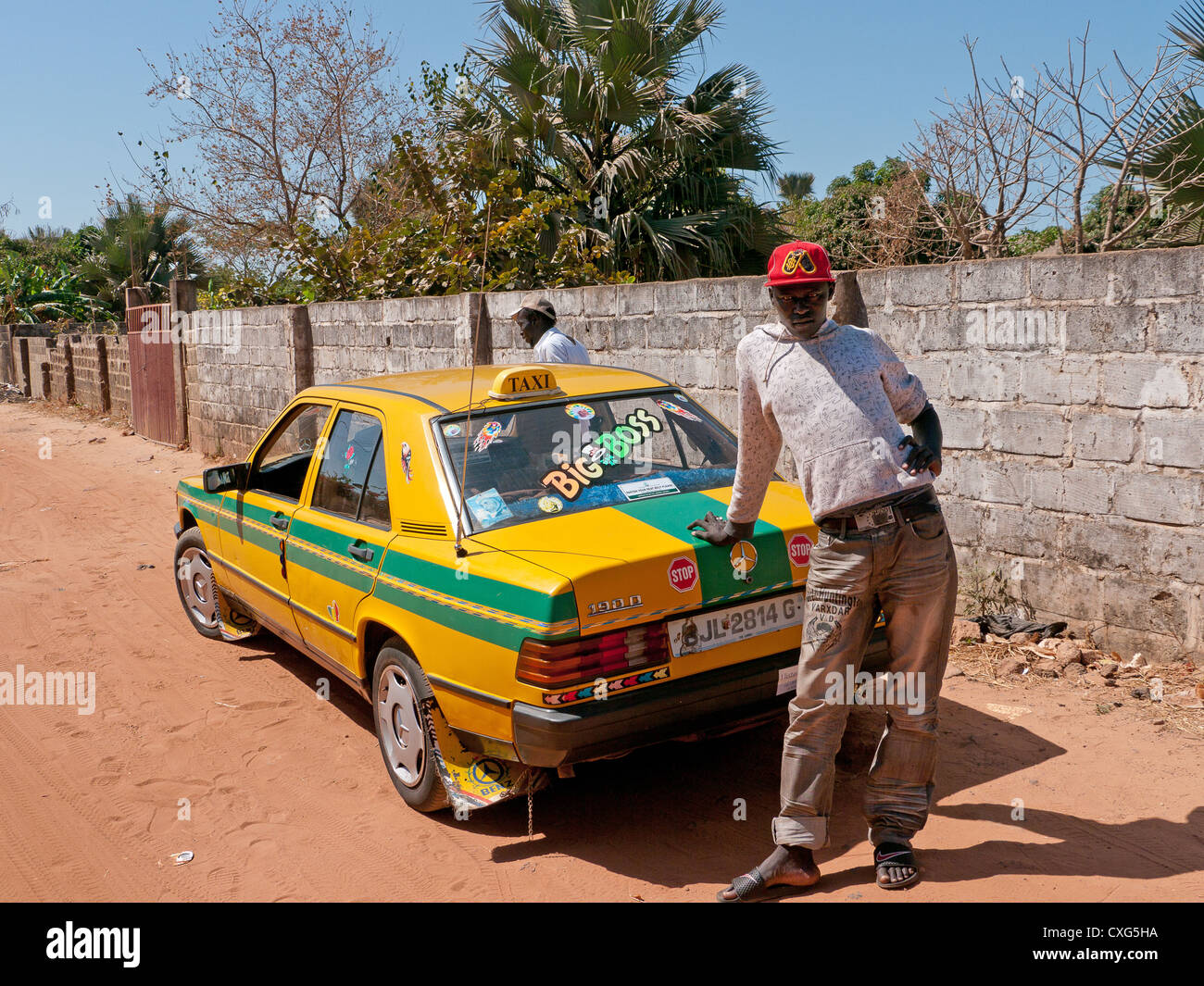 Two men and their yellow taxi on a road in Gambia, Africa Stock Photo