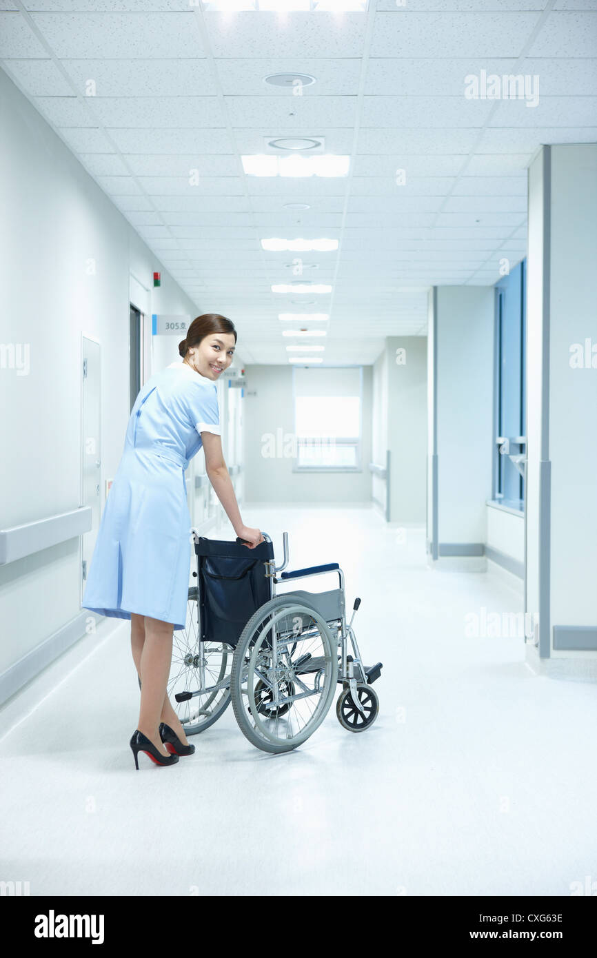 A nurse walking with an empty wheelchair in hospital corridor while ...