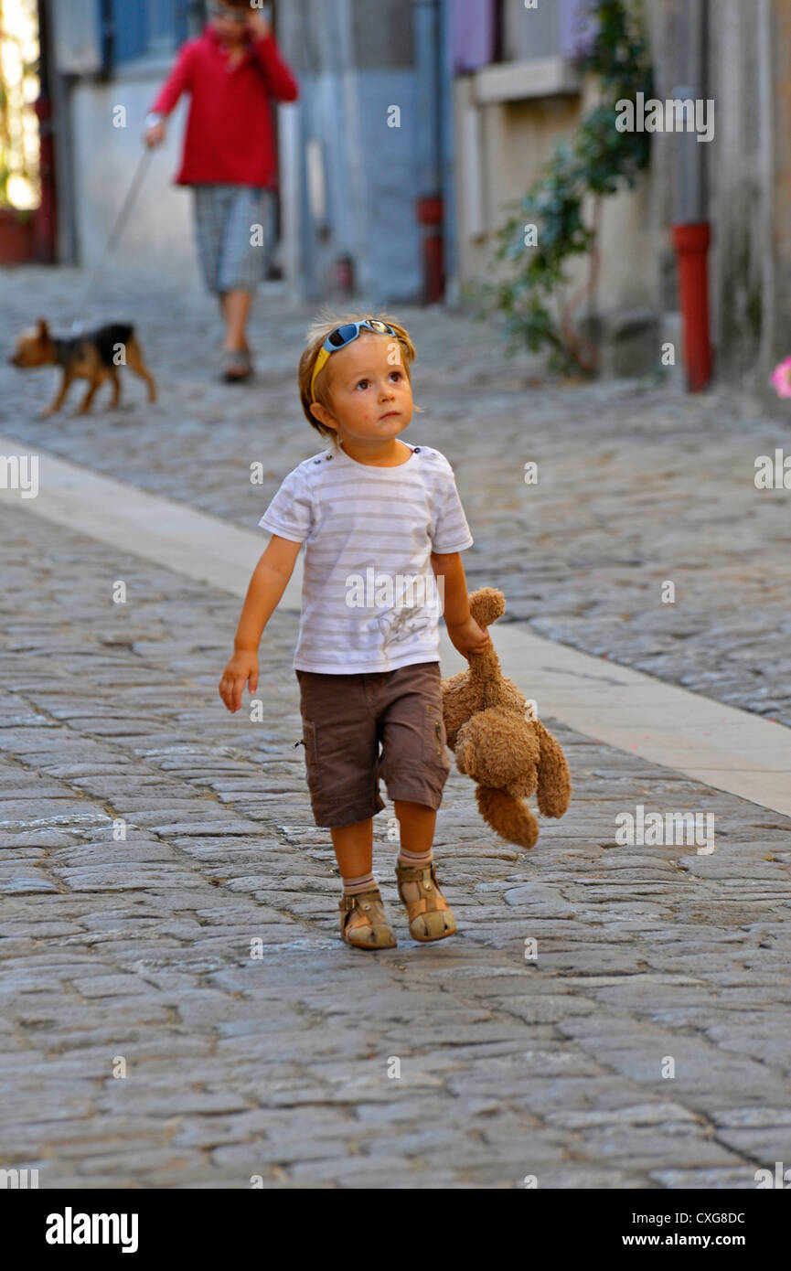 Young boy walking in street clutching a cuddly toy. Stock Photo
