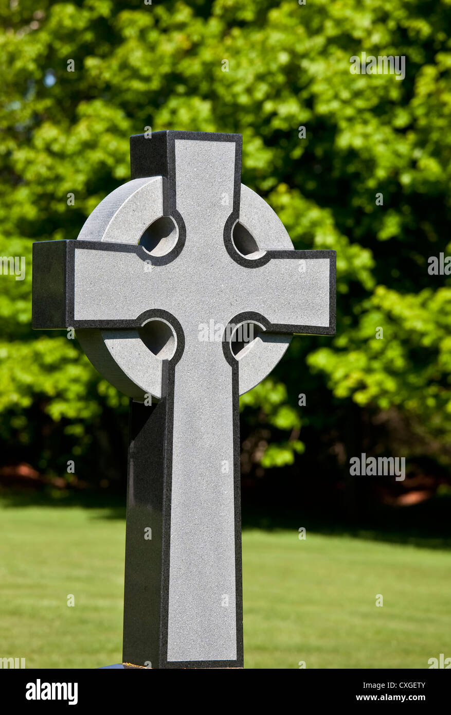 Modern stylized Celtic cross monument with a background of trees. Stock Photo