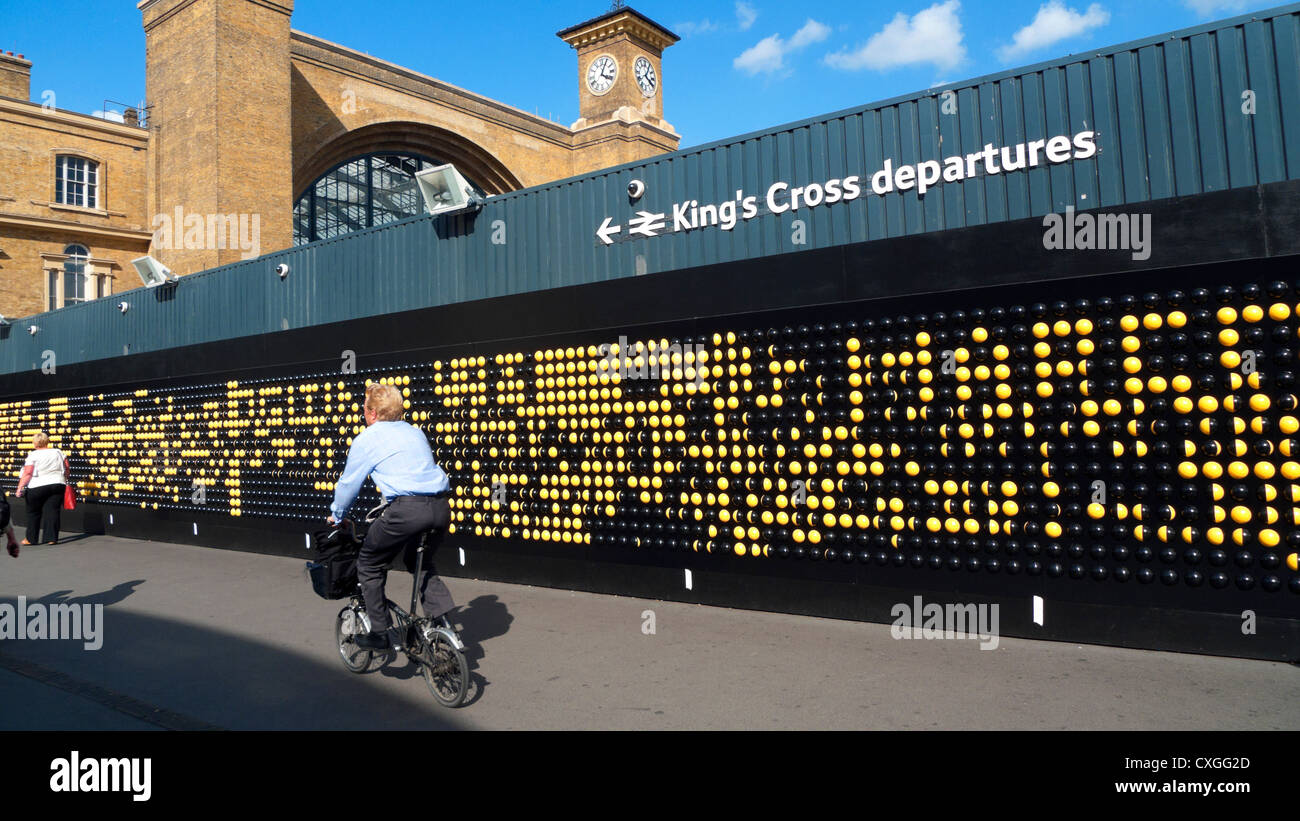 Commuter man cycling past the Song Board interactive art installation at King's Cross Train Station on a Brompton bike in London UK  KATHY DEWITT Stock Photo