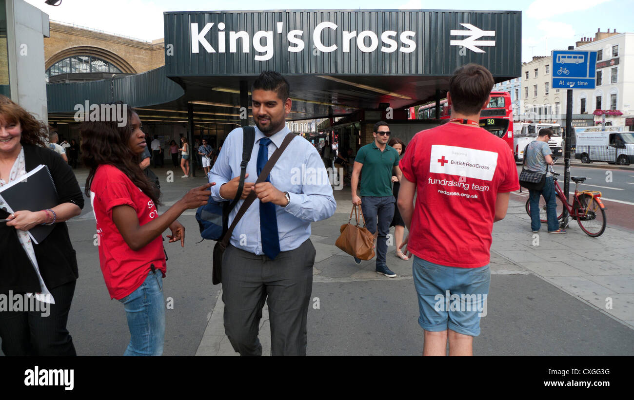 Red Cross charity worker fundraising talking to a businessman collecting donations on the street outside King's Cross Station London UK   KATHY DEWITT Stock Photo