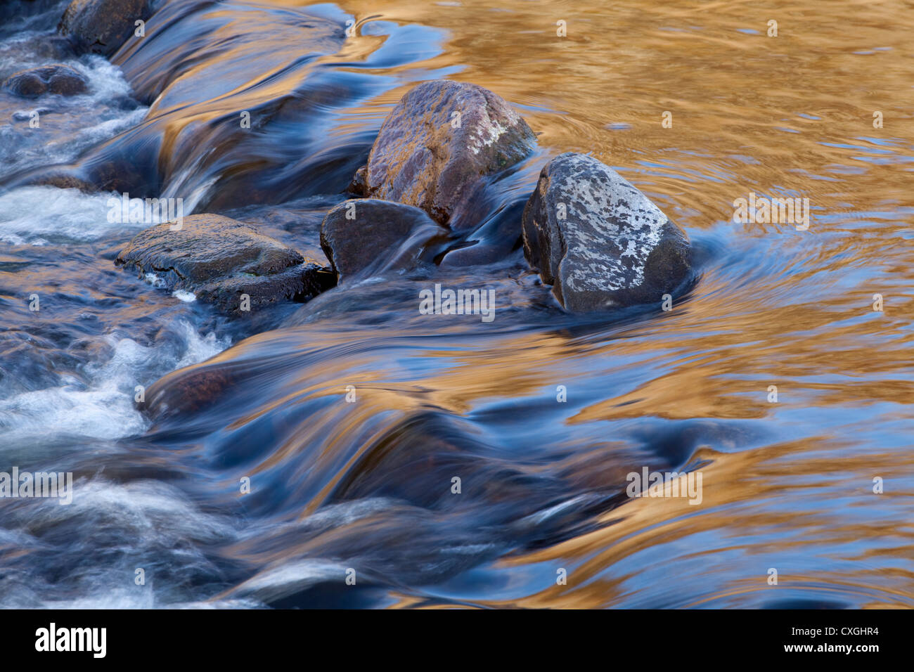 A golden sunset reflected into a small waterfall on the River Breamish in Northumberland, UK Stock Photo