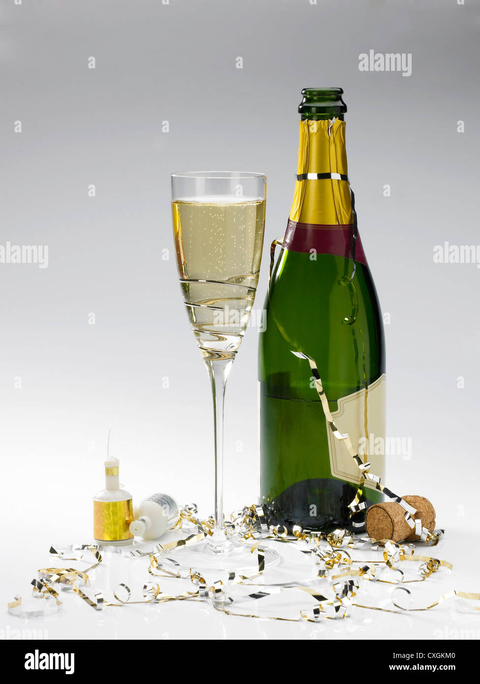 a champagne bottle, glass of champagne, streamers and poppers on a graduated grey background Stock Photo