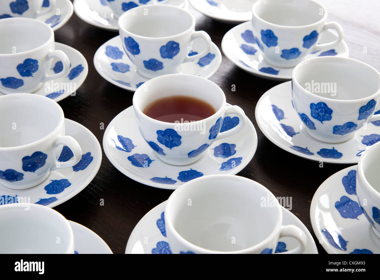 One cup of tea in blue and white teacup, surrounded by empty teacups. Stock Photo