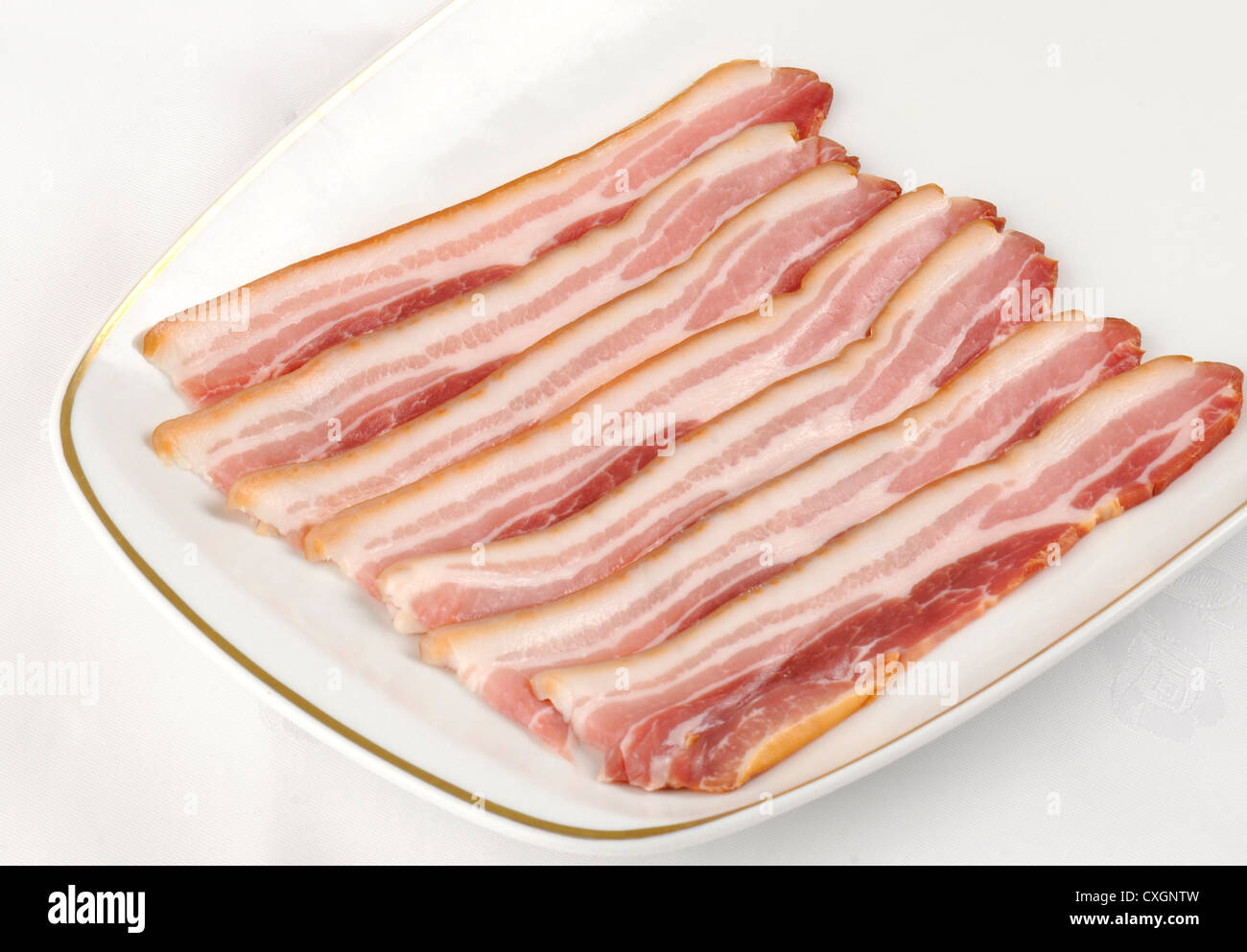 a white plate with strips of uncooked smoked streaky bacon Stock Photo