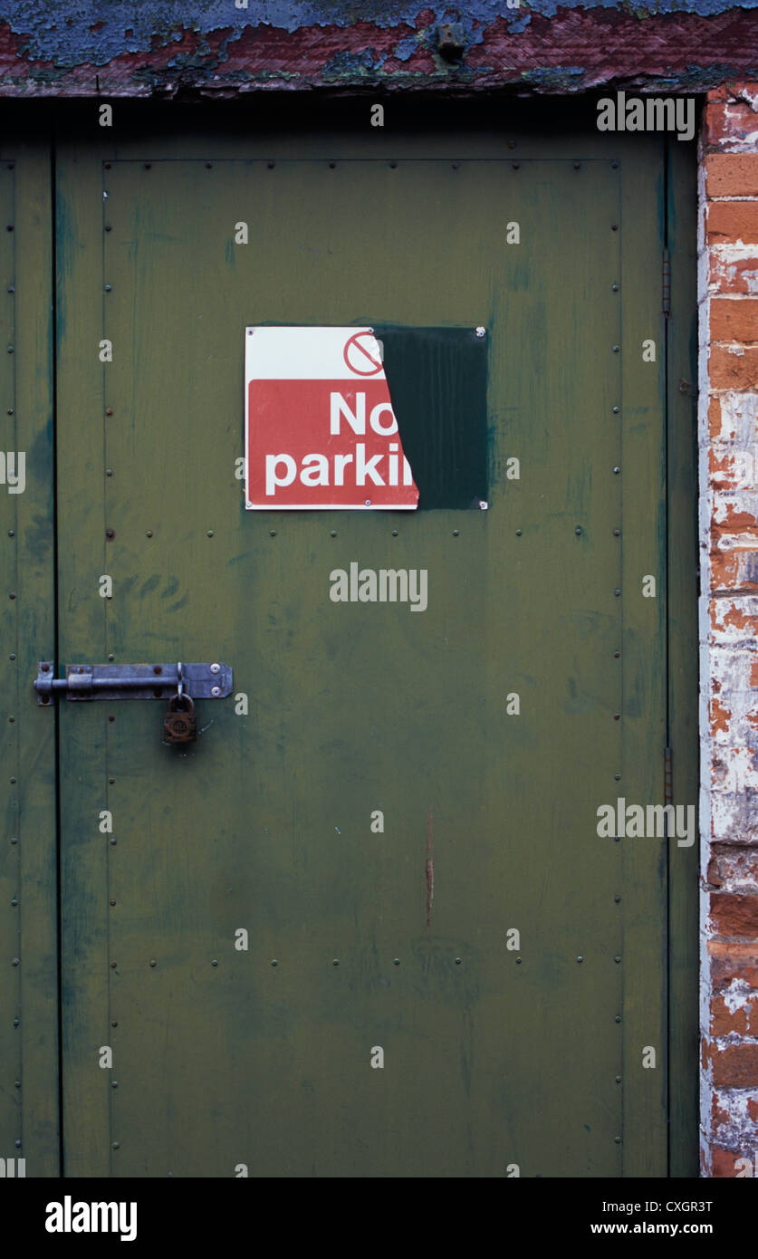 Strengthened security door bolted and padlocked but needing painting with sign half ripped off stating No Parking Stock Photo