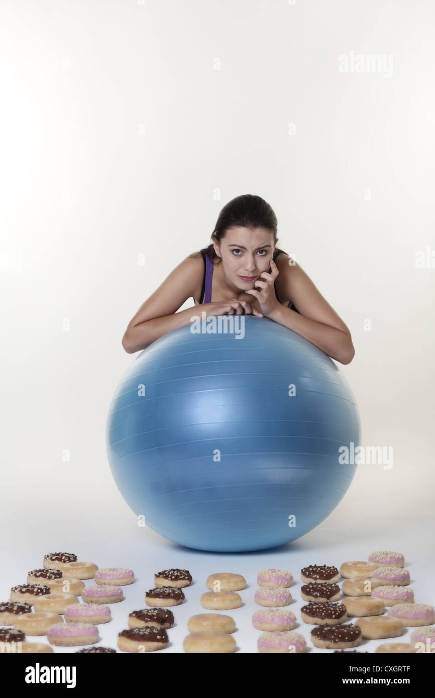 attractive woman looking over a exercise gym ball at many donuts unsure what to do the temptation is just to much Stock Photo