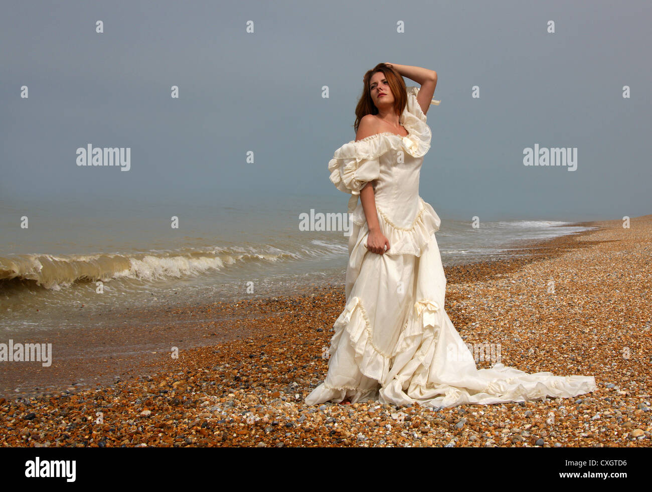 Girl Wearing a Cream White Wedding Dress on a Shingle Beach by the Sea. Stock Photo