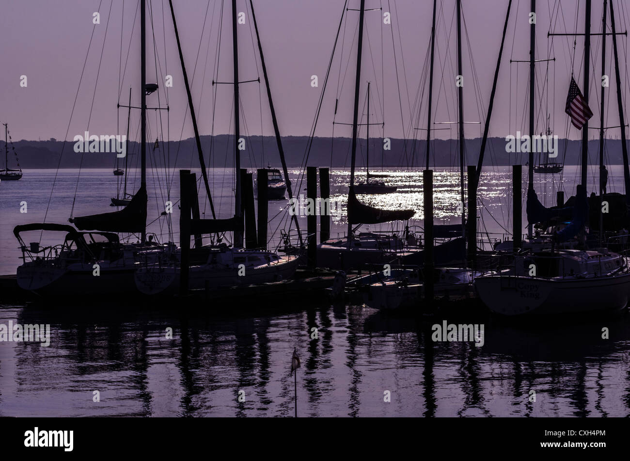 Docked sailboats silhouetted against a purple sky at sunrise. Sunlight shimmers on the water. Niantic East Lyme Connecticut USA Stock Photo