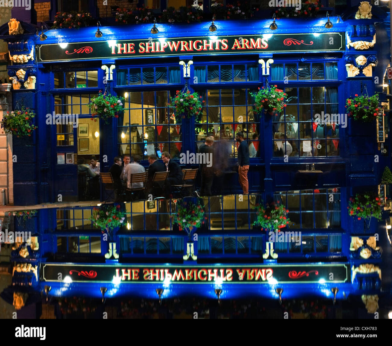 The Shipwright Arms on Tooley Street London reflected in a  water feature with City workers drinking outside at night Stock Photo