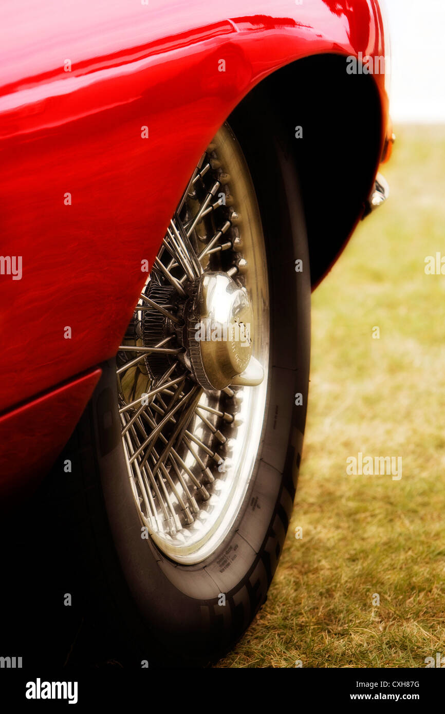 Wheel detail of red E-Type Jaguar showing chrome spokes, parked on grass Stock Photo