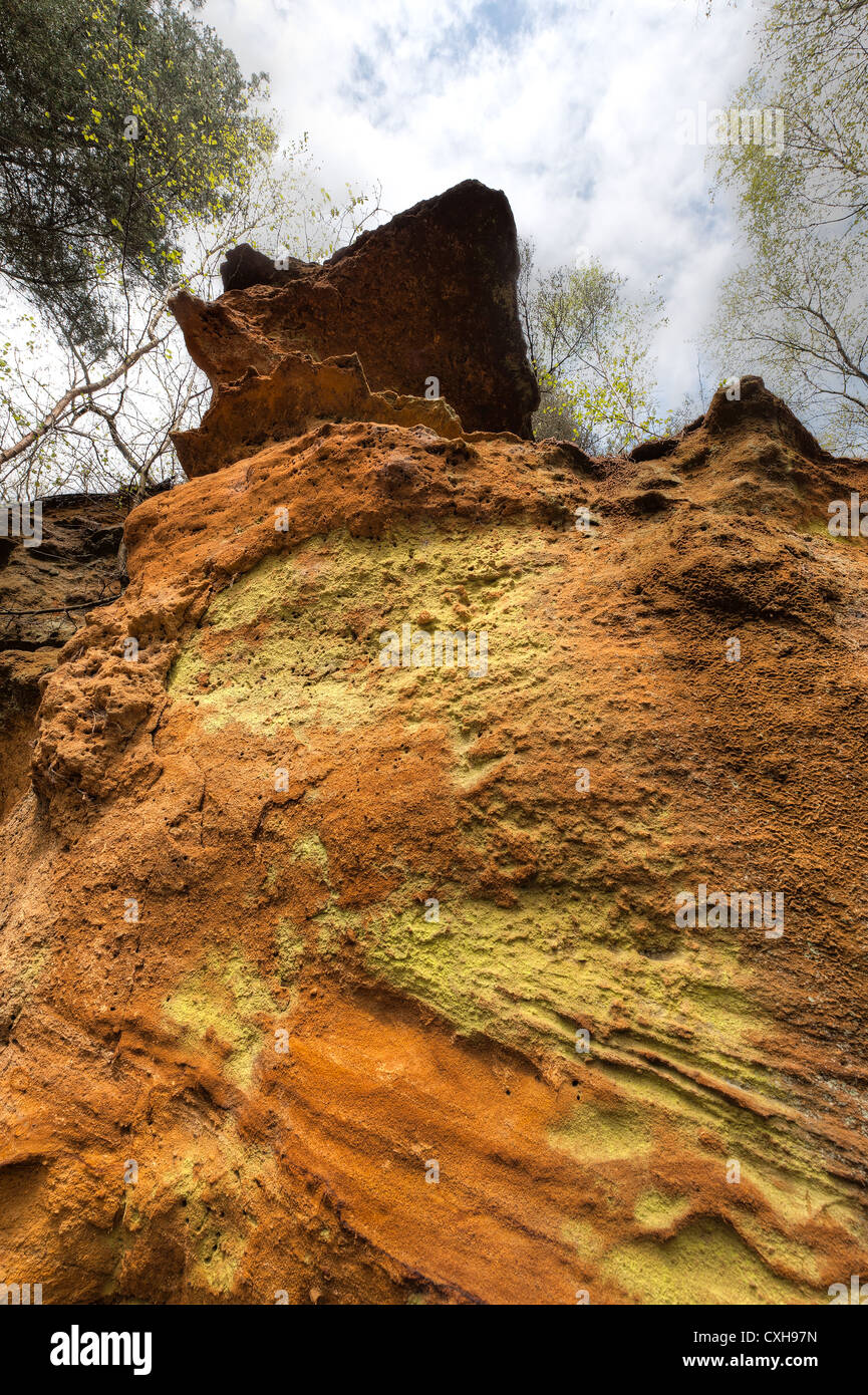Greensand Ridge sandstone deposits as differing layers and rich orange colors at the foot of a steep secluded cliff face Stock Photo