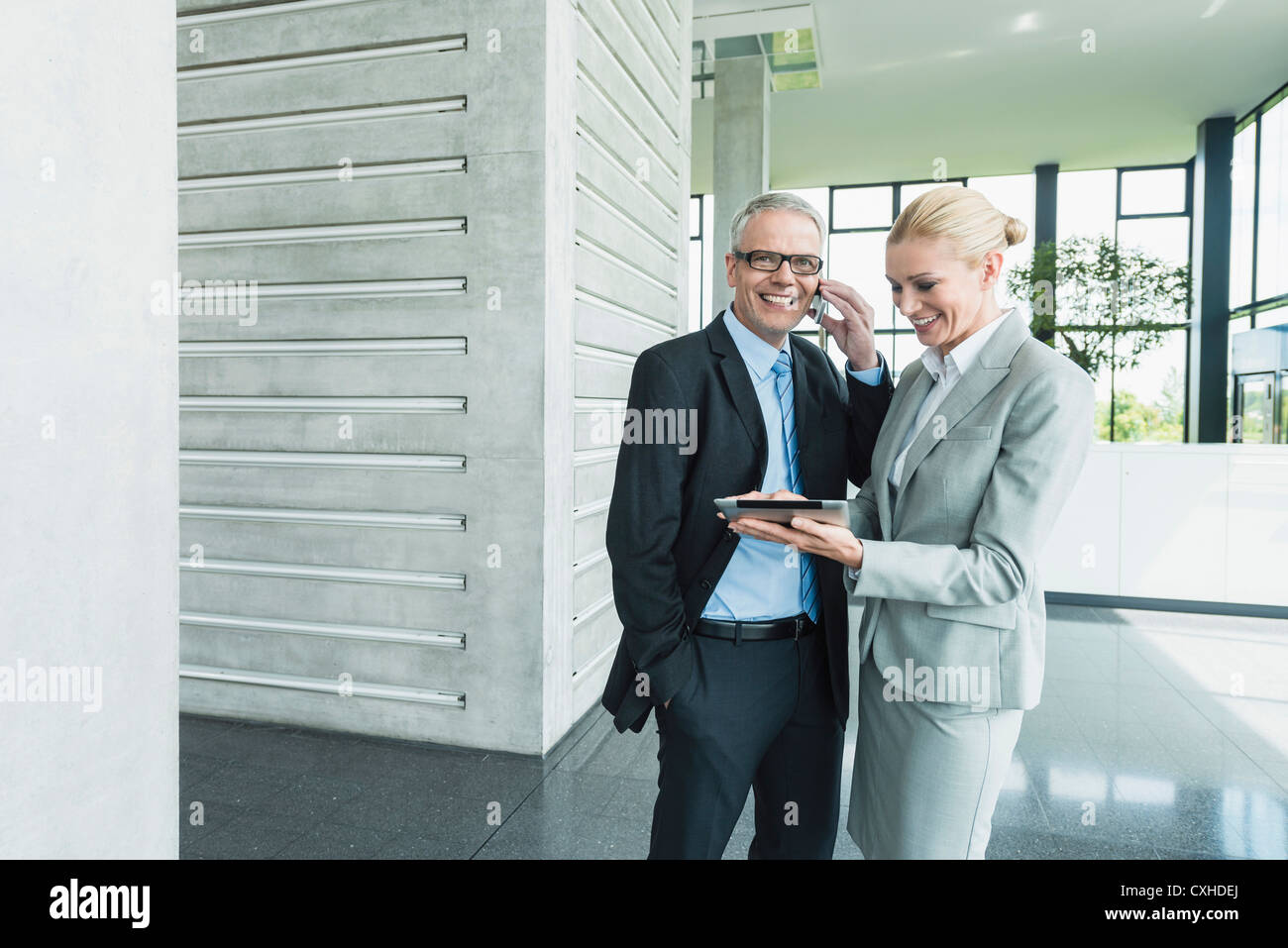 Germany, Stuttgart, Businesswoman with digital tablet while man talking on phone Stock Photo