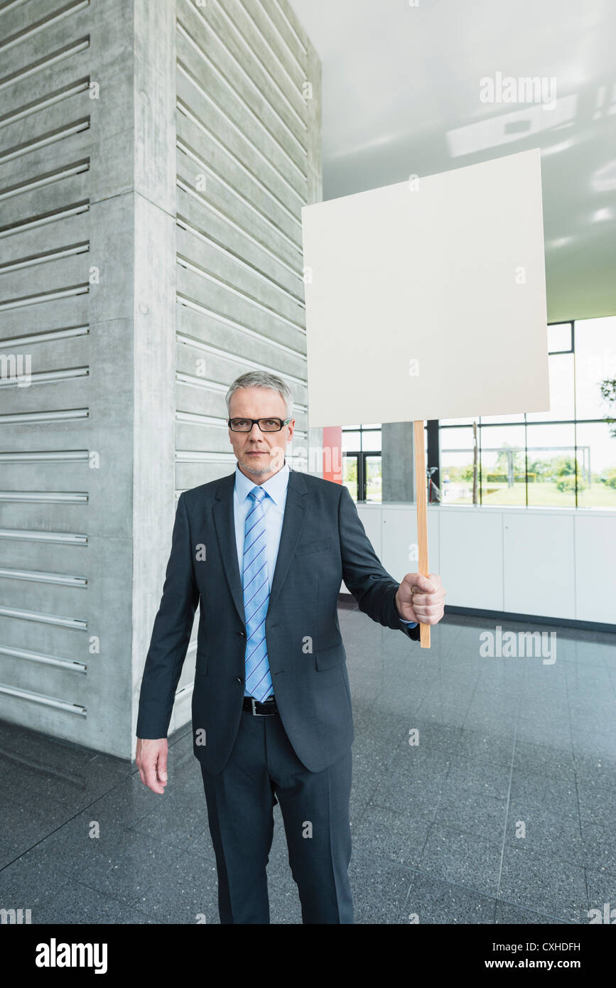 Germany, Stuttgart, Businessman holding placard in office lobby Stock Photo