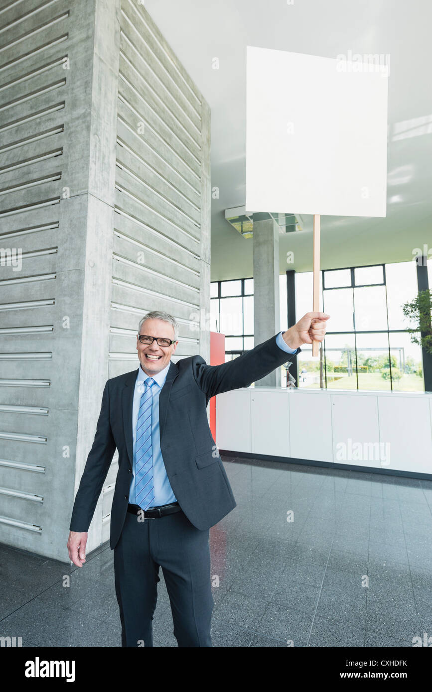 Germany, Stuttgart, Businessman holding placard in office lobby Stock Photo