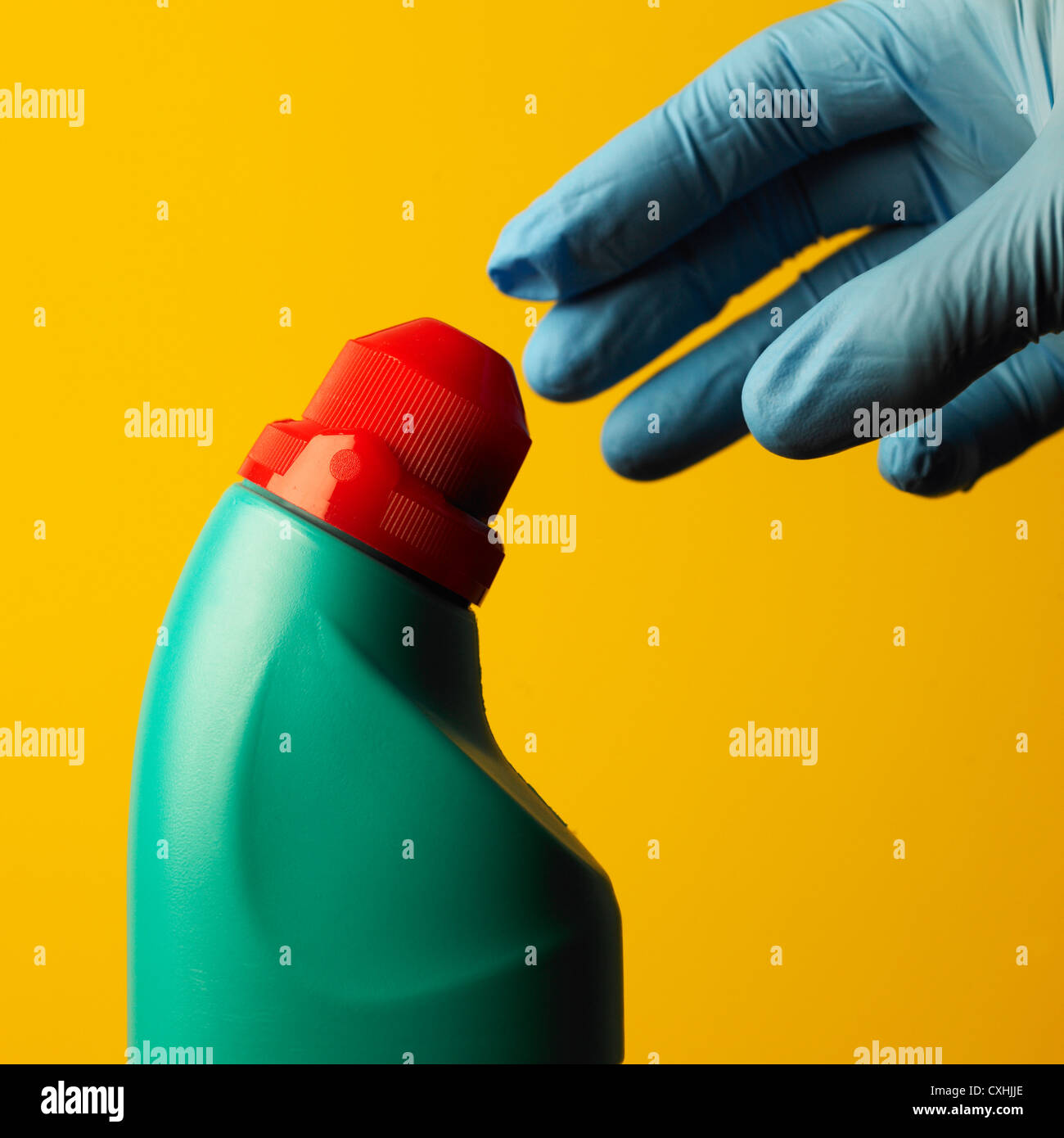 Hand in blue household glove reaching green plastic cleaning bottle