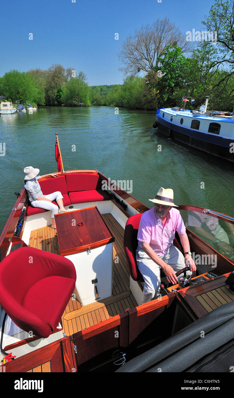 Couple cruising on a gentlemans motor yacht or motorboat on the  upper reaches of the River Thames, Pangbourne, Berkshire, England, UK Stock Photo