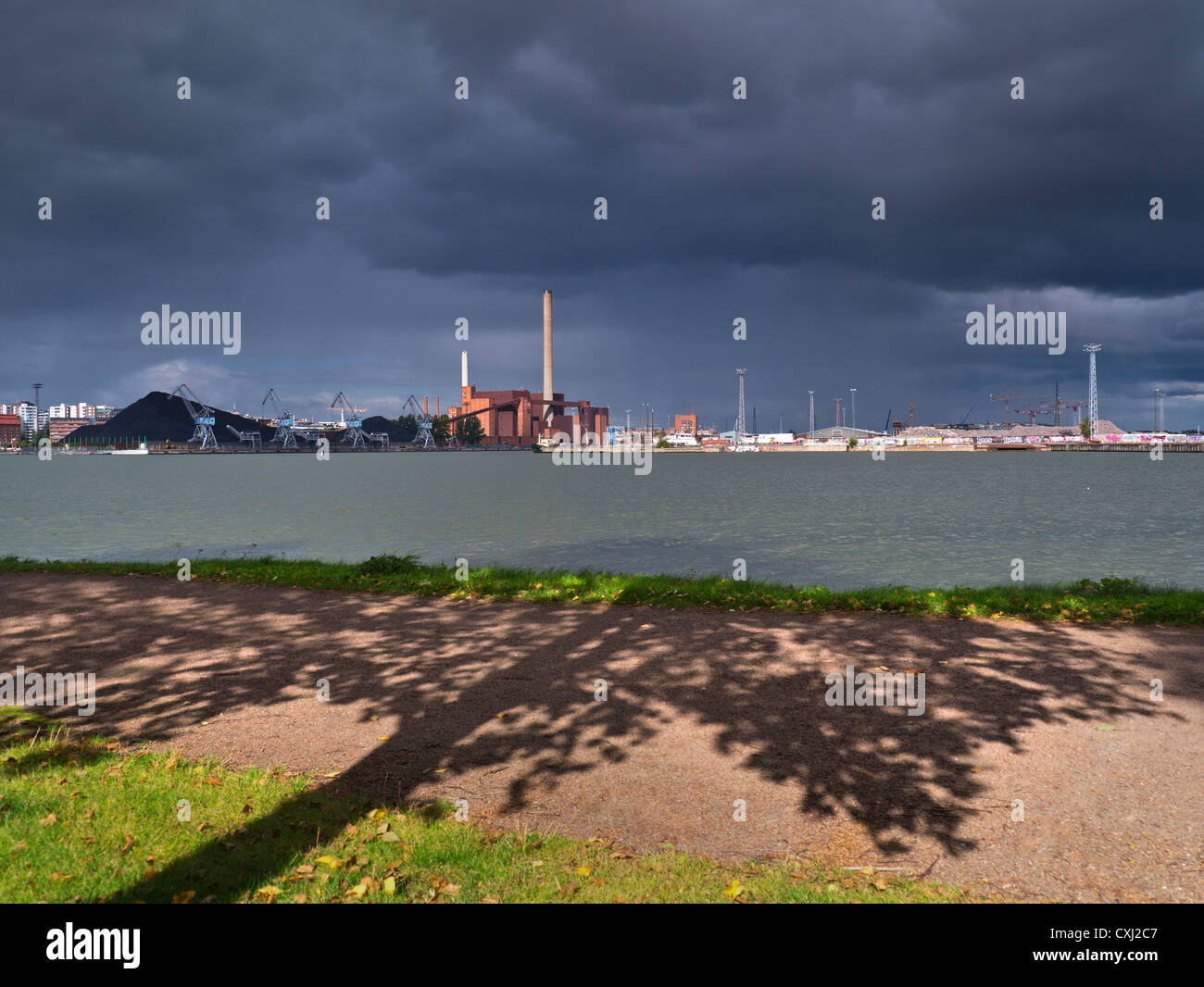 Coal fired power station fossil fuel old technology under dramatic sky with tree and leaves silhouetted in foreground contrasting greener better way Stock Photo