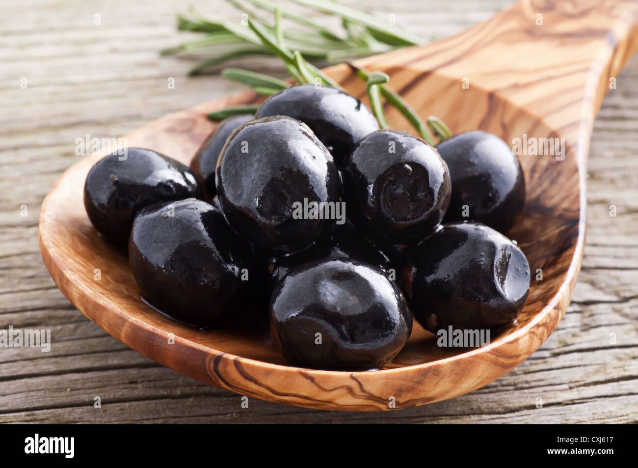 Black pickled olives on a olive wood spoon as closeup on old wood Stock Photo