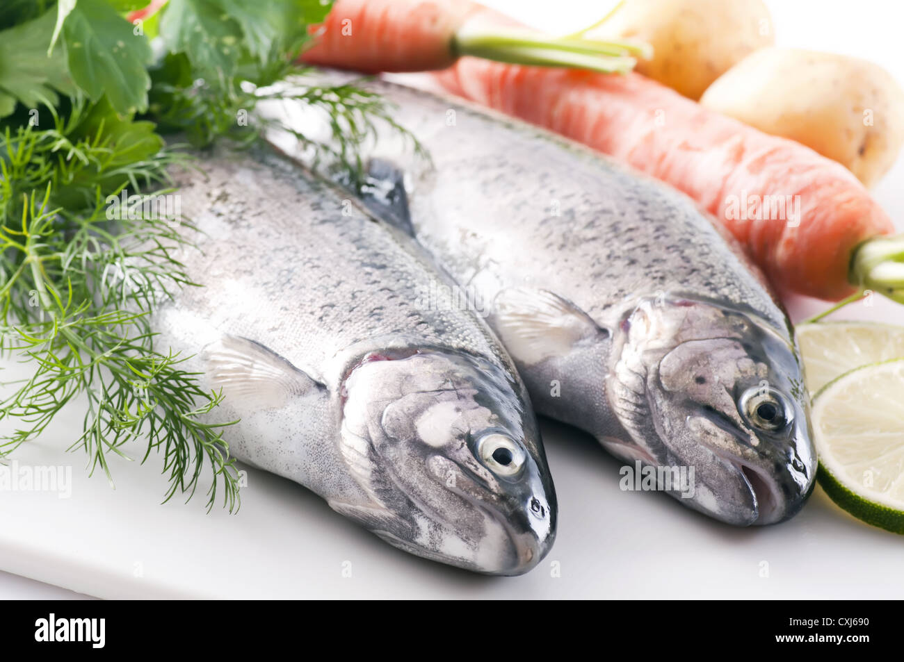 Two fresh rainbow trout with potatoes, vegetables and herbs as closeup on white background Stock Photo