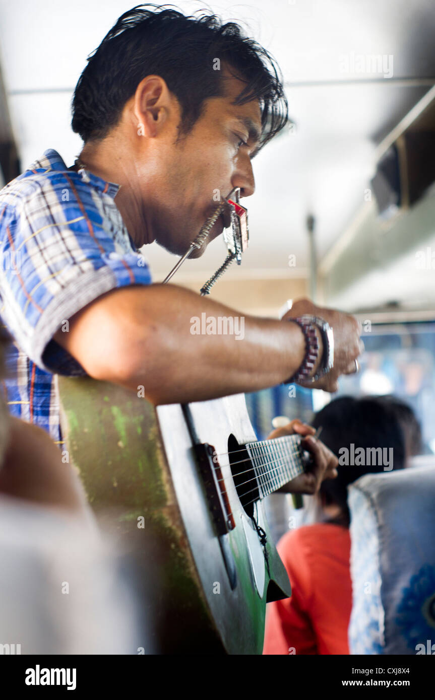 An indonesian man busking by singing in the bus, asia scene. Slight motion shakes are visible at 100% zoom. Stock Photo
