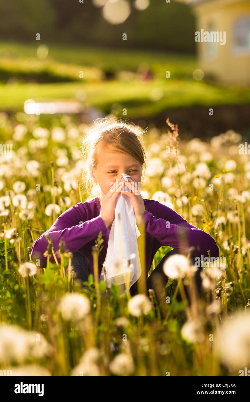 Girl sitting in a meadow with dandelions and has hay fever or allergy Stock Photo