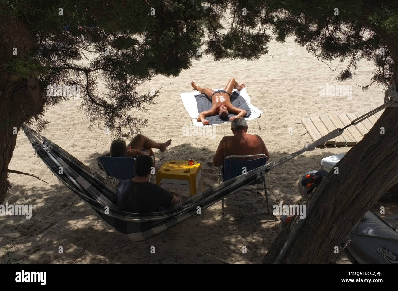 Three people in the shade of the sun whilst a fourth lies on the beach Stock Photo